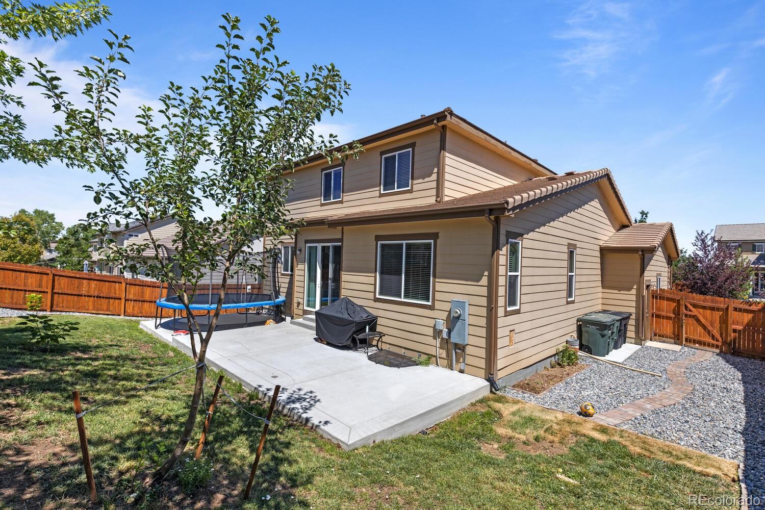 Rear of a tan two-story home with a fenced yard, concrete patio, and above-ground trampoline.