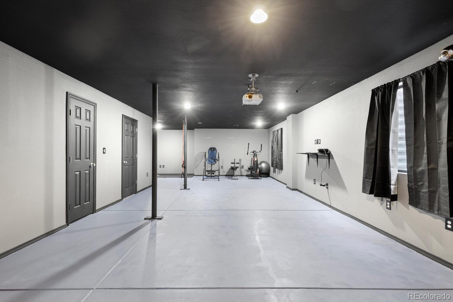 Home gym with exercise equipment, a ceiling-mounted projector, and a black ceiling.