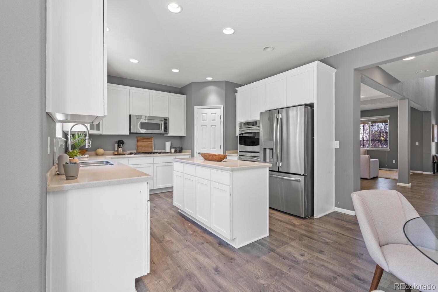 Bright kitchen with white cabinets, a central island, stainless steel appliances, and wood-look flooring.