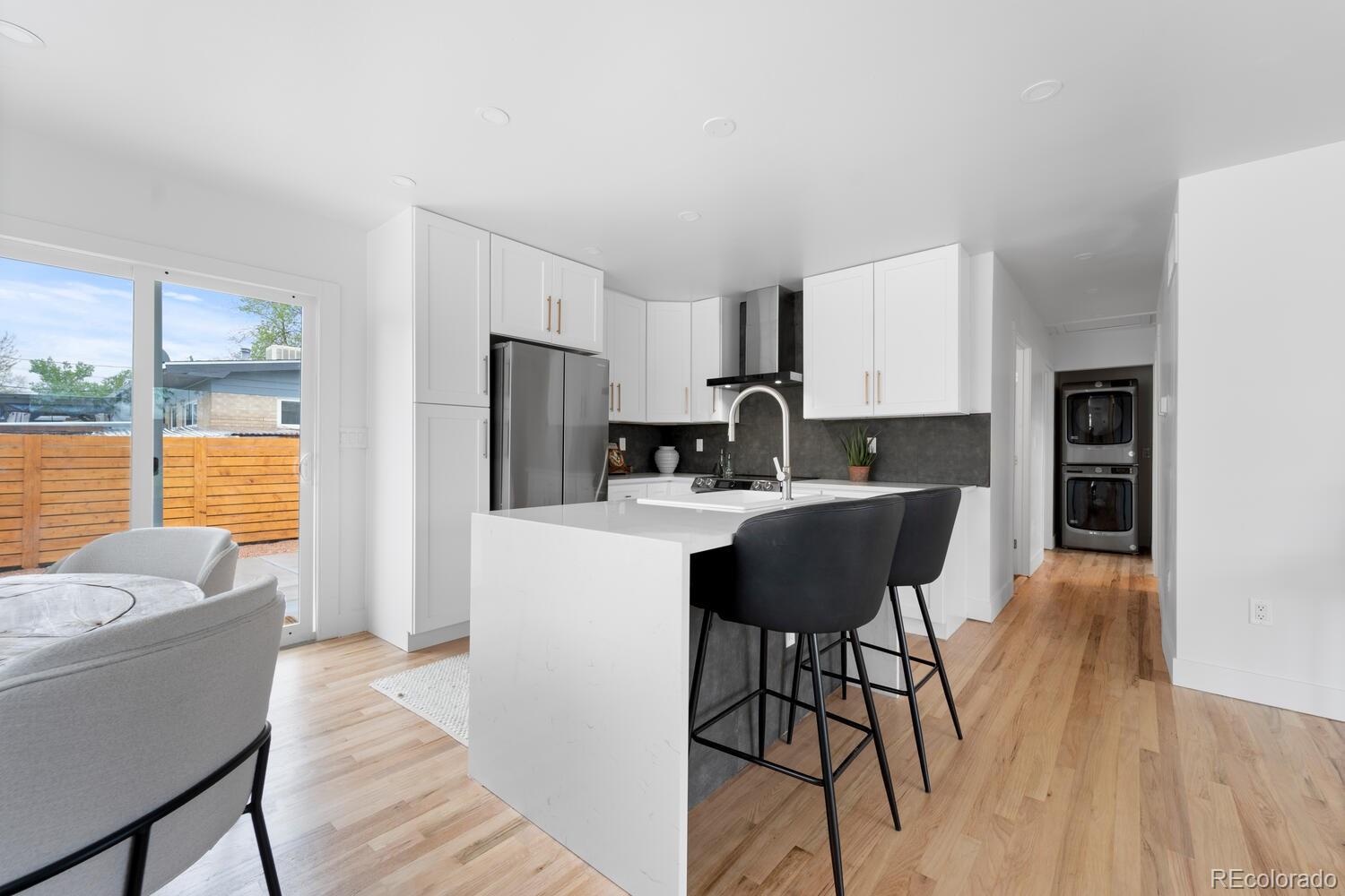Open-plan kitchen with white cabinets, a large island, dark bar stools, and sliding doors to a fenced patio.