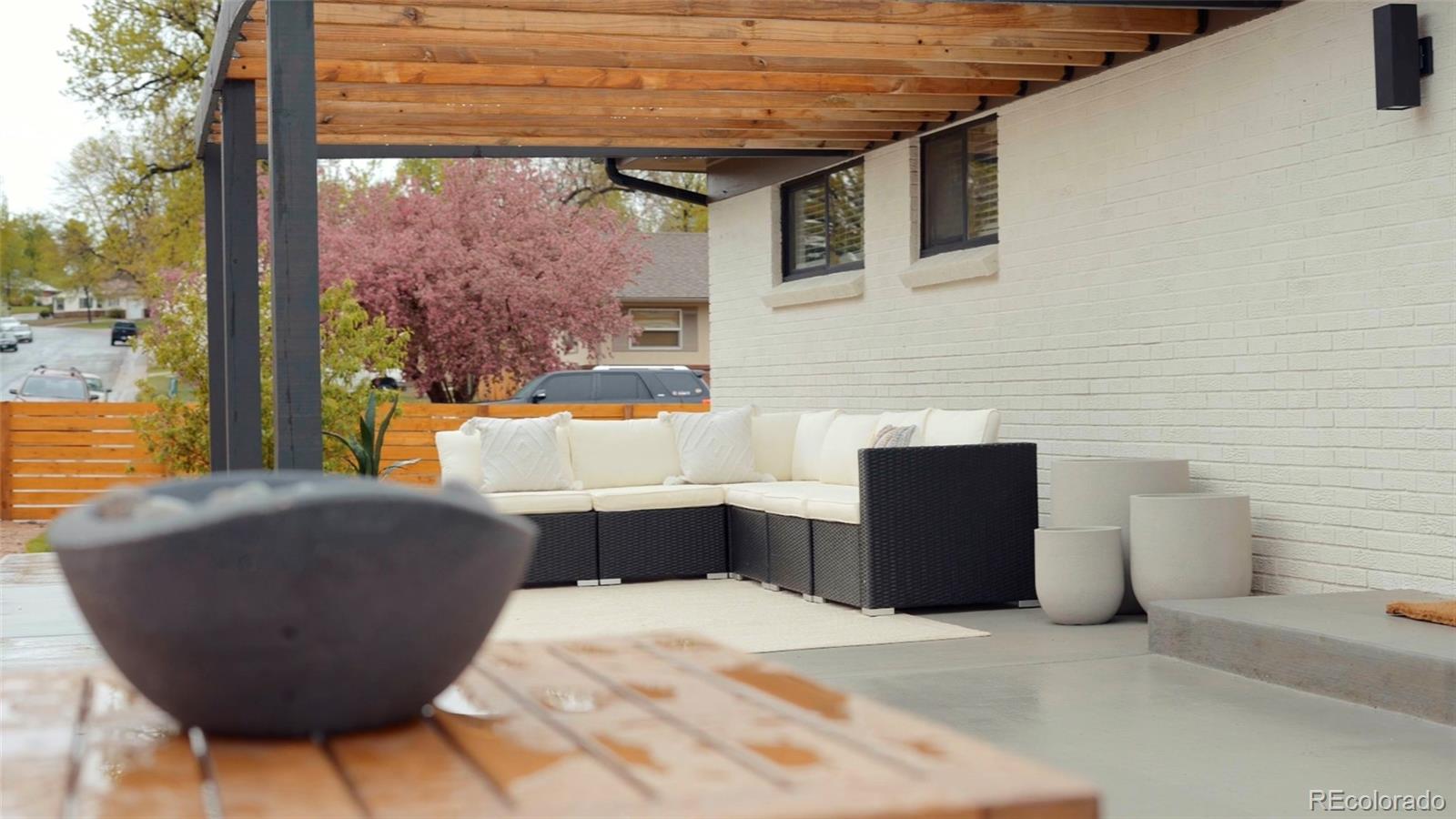 Covered patio with a timber pergola, white brick wall, and white-cushioned sectional sofa.