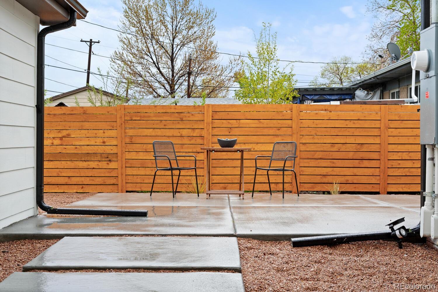 Concrete patio with two metal chairs and a table, enclosed by a tall cedar privacy fence.