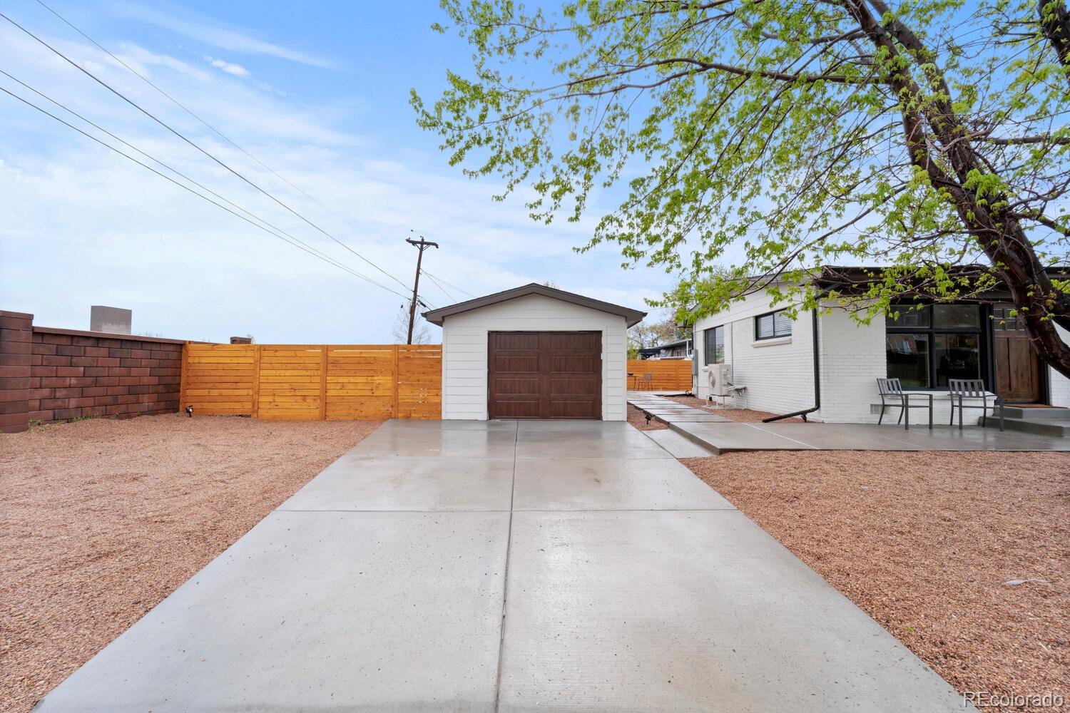 Backyard with detached garage, broad concrete driveway, wooden fence, and patio chairs beside the house.