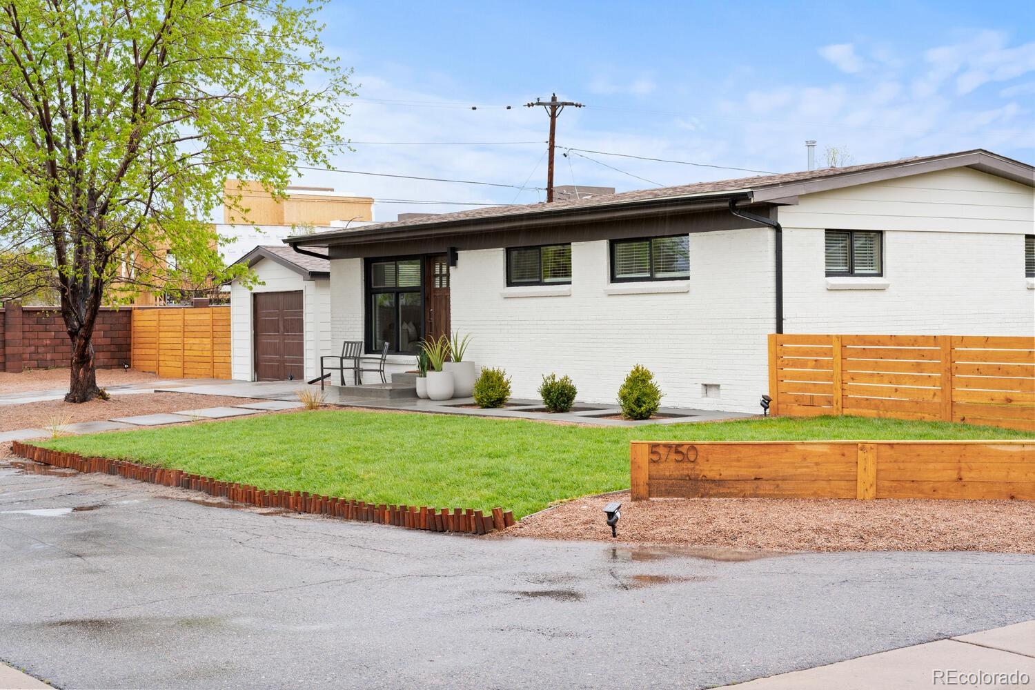 Single-story white brick home with a covered patio, green lawn, and wooden fencing.