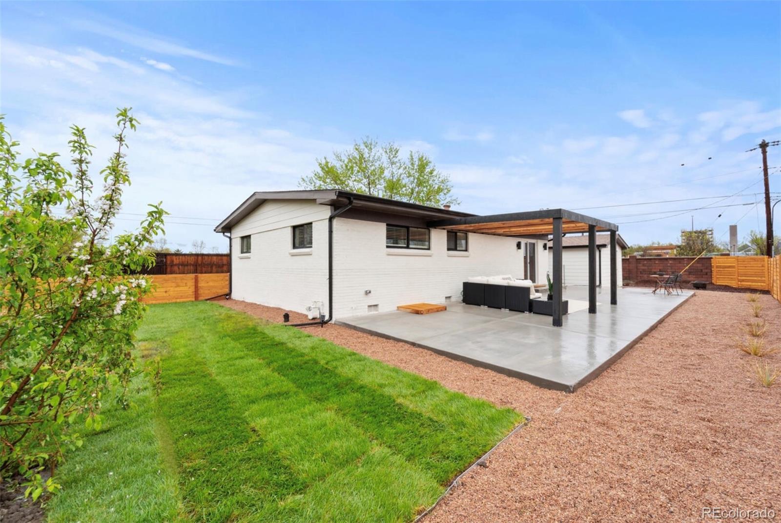 White brick home with a covered patio and pergola overlooking a green lawn and fenced yard.