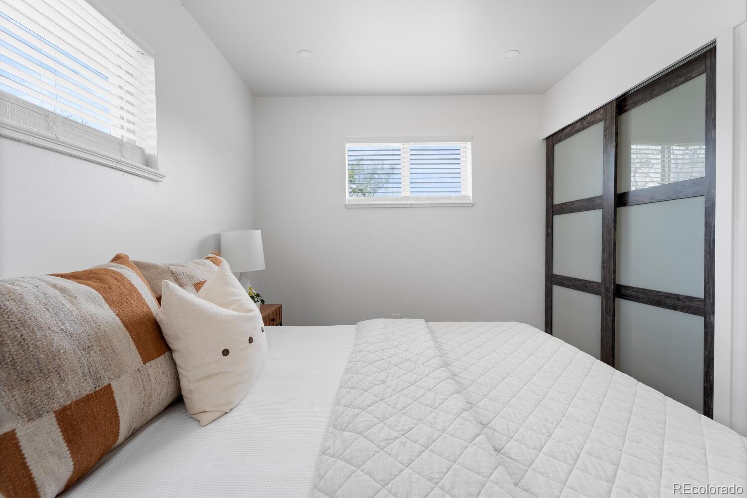Bedroom with a white quilted bed and dark wood-framed frosted glass closet doors.