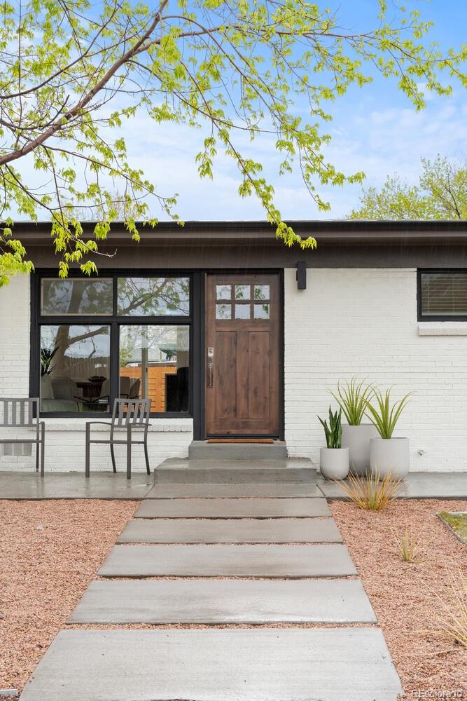 White brick home entrance with a wood door, concrete walkway, and gravel landscaping.