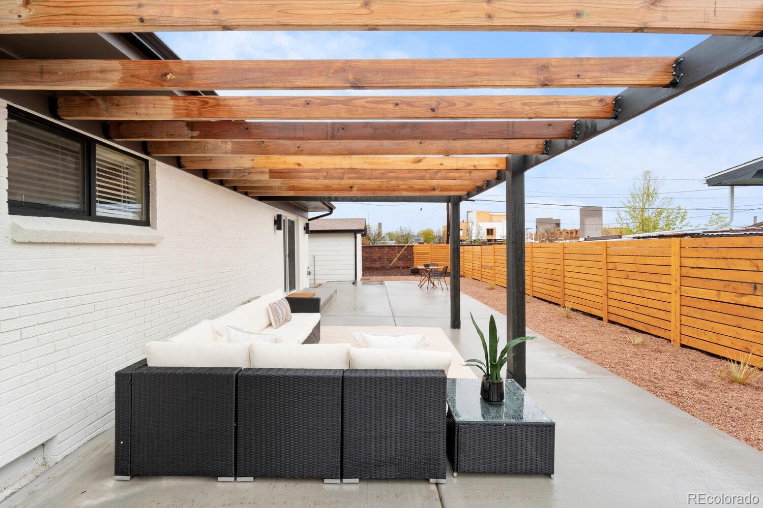 Covered backyard patio with a timber pergola, white sectional seating, and cedar privacy fence.
