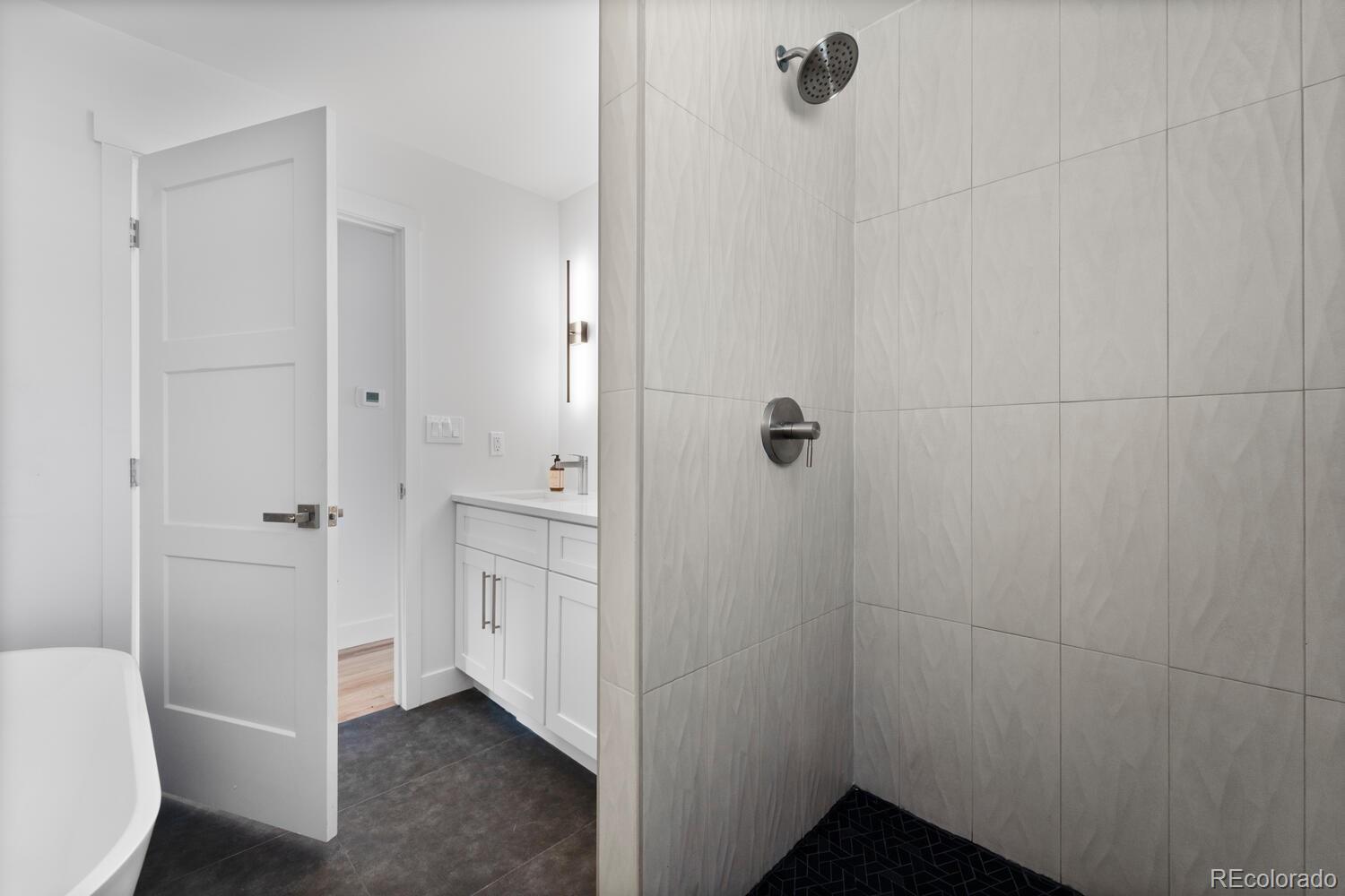 Bathroom with a large tiled walk-in shower, white vanity, and edge of a freestanding tub.