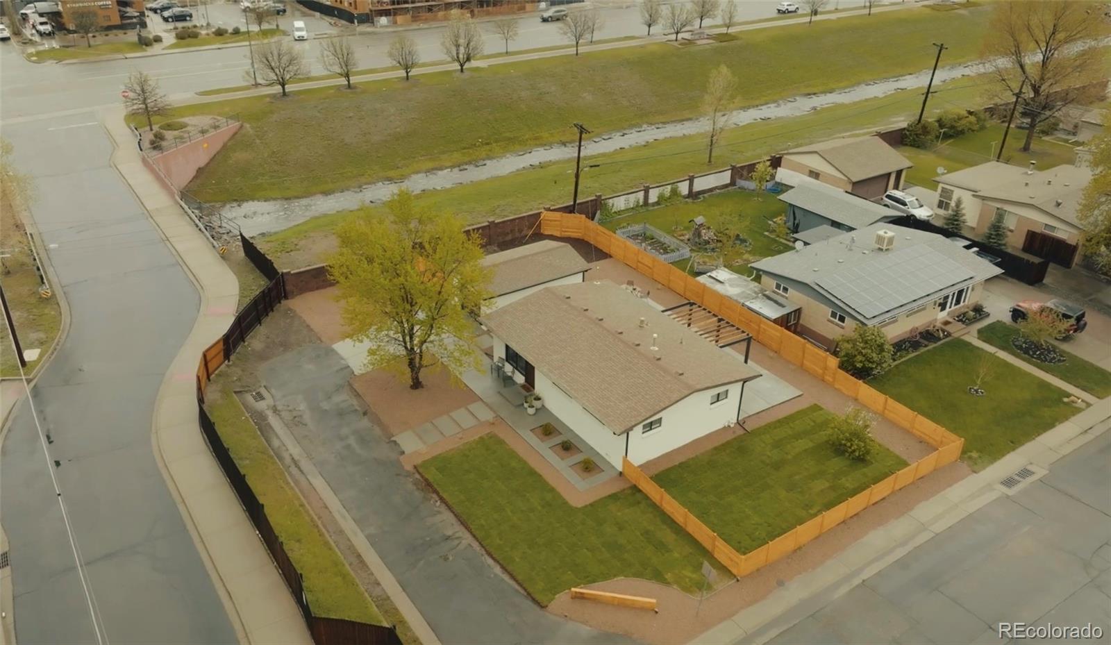 Aerial view of a single-story home with a fenced yard beside a road and drainage channel.