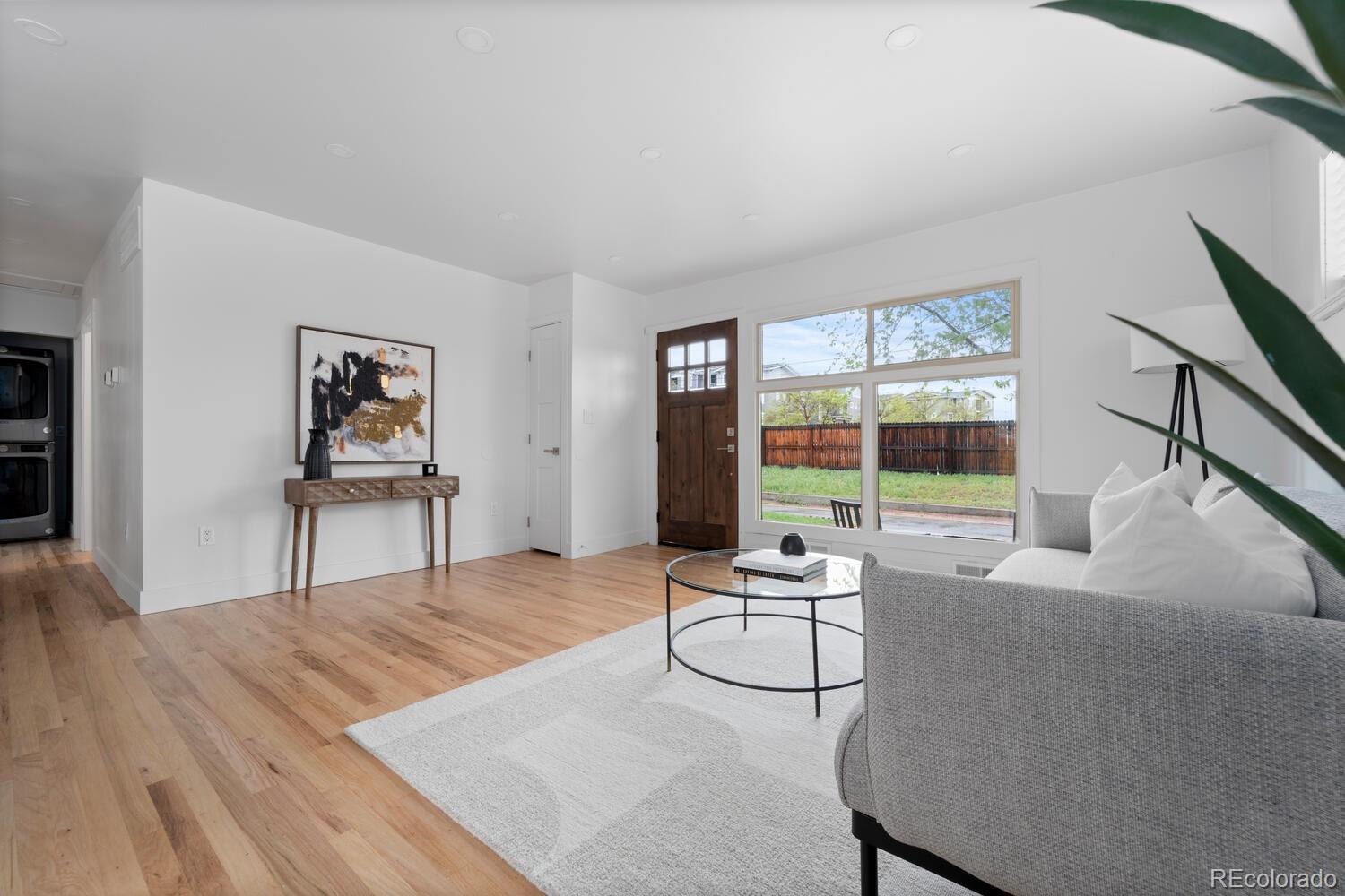 Living room with hardwood floors, a gray sofa, and large windows overlooking a fenced yard.