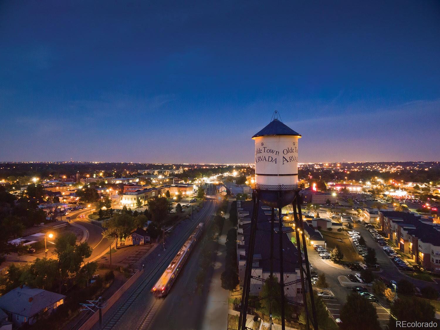 Aerial view of Olde Town Arvada at night, with the water tower above illuminated streets and railway tracks.