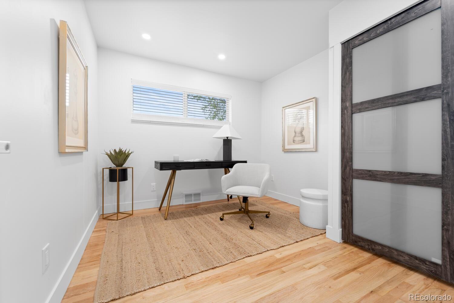 Home office with a black desk, white chair, woven rug, and dark-framed sliding door.
