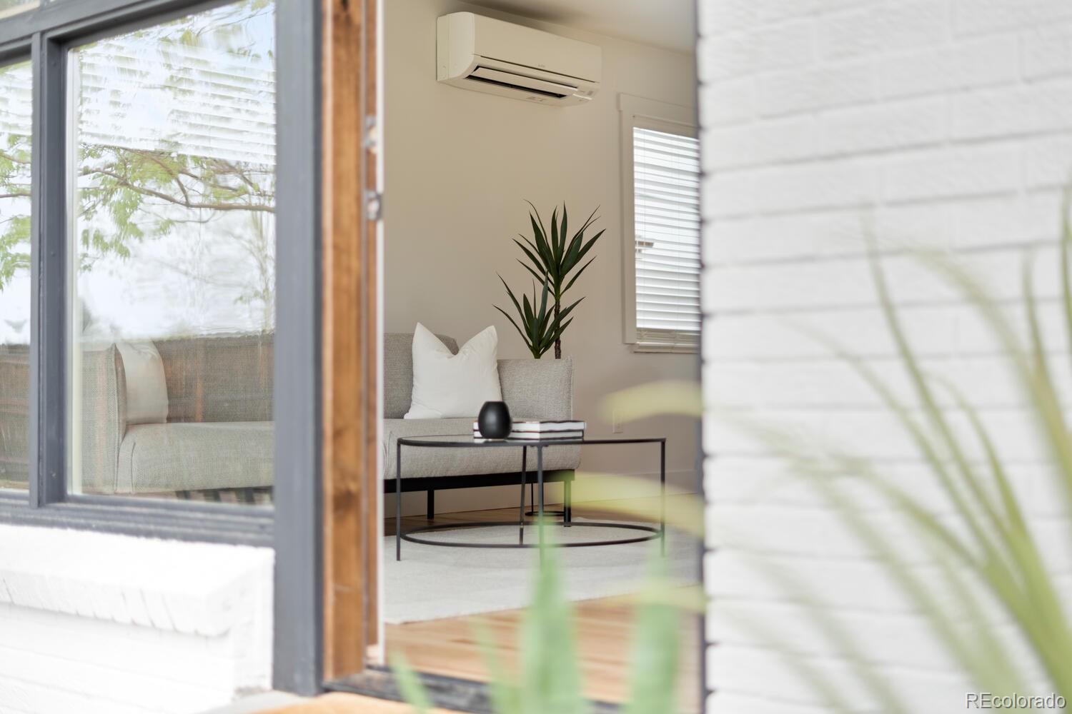 Living room with a gray sofa, black oval coffee table, potted plant, and wall-mounted air conditioner.
