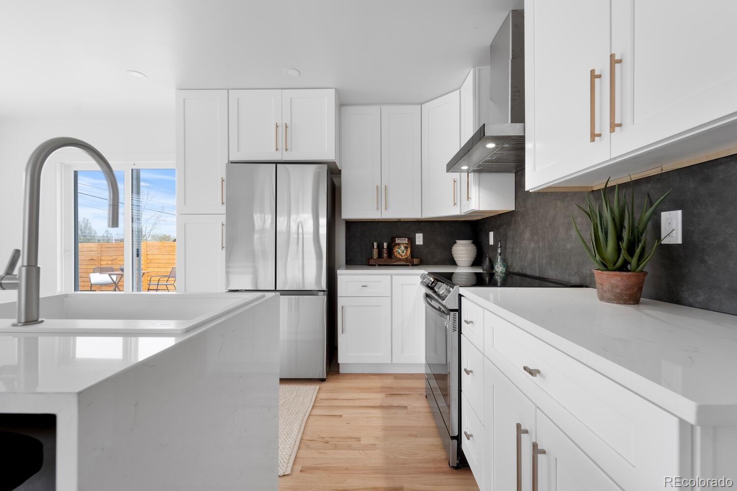 Bright white kitchen with a large island, stainless steel appliances, and a dark backsplash.