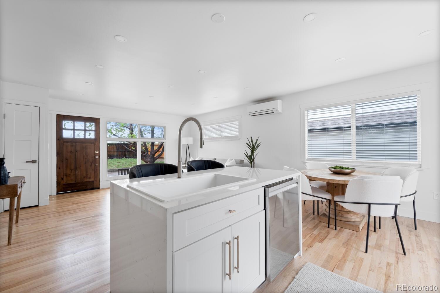 Open kitchen and dining area with a large white island, wood floors, and a wooden front door.