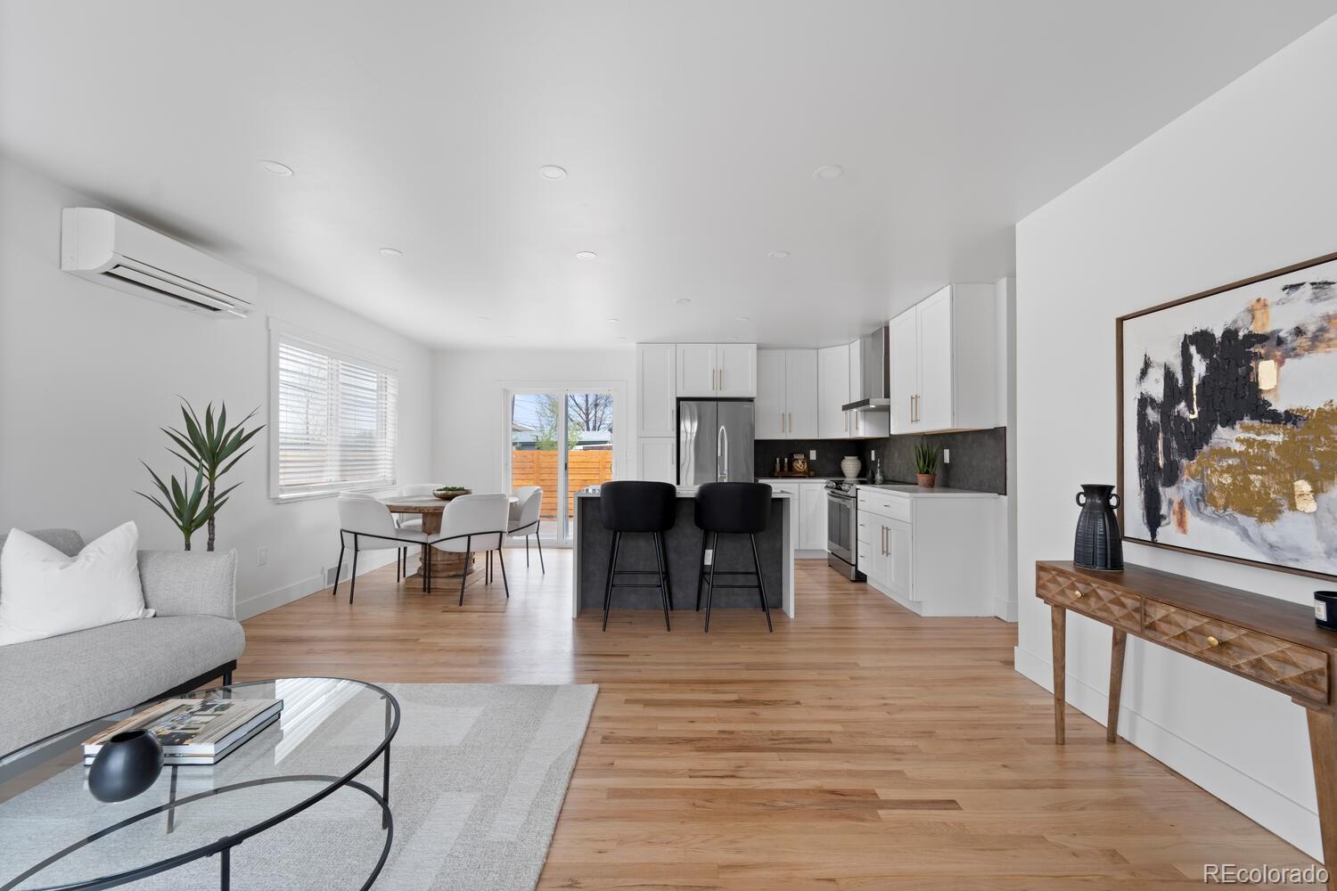 Open-plan living room and kitchen with white cabinets, a dark island, and hardwood floors.