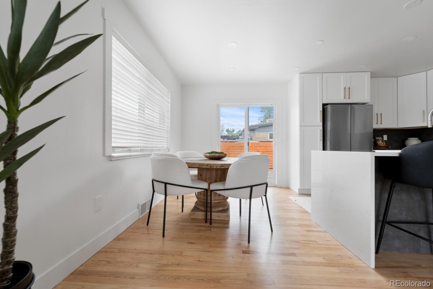 Dining area with a round wood table beside a white kitchen and sliding glass doors.