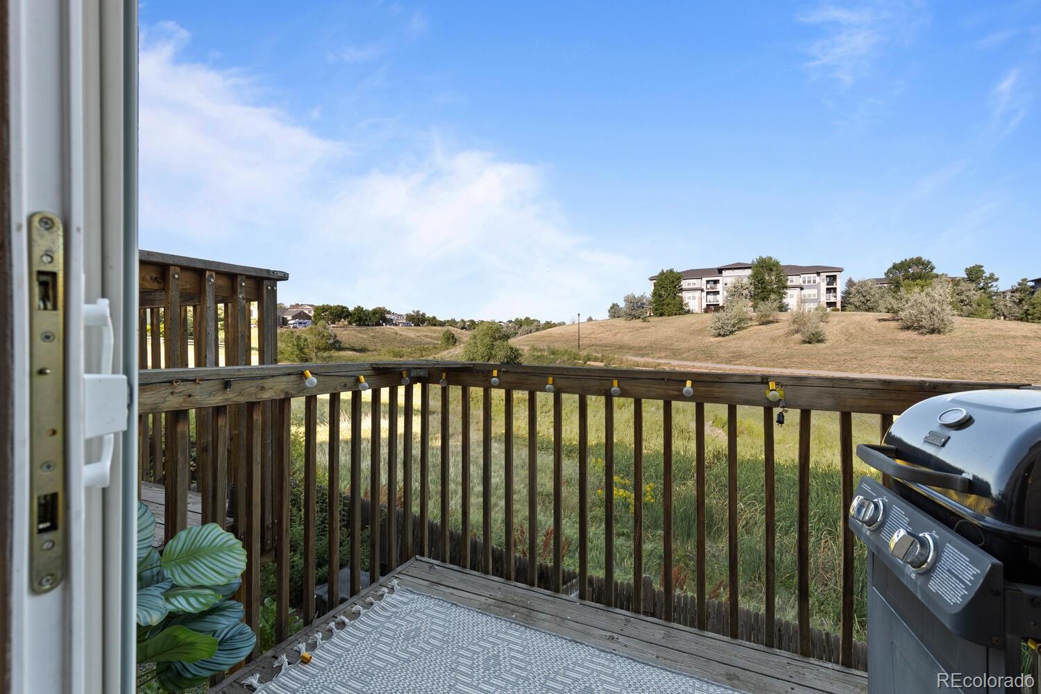 Wooden deck overlooking grassy hills, with string lights and a barbecue grill.
