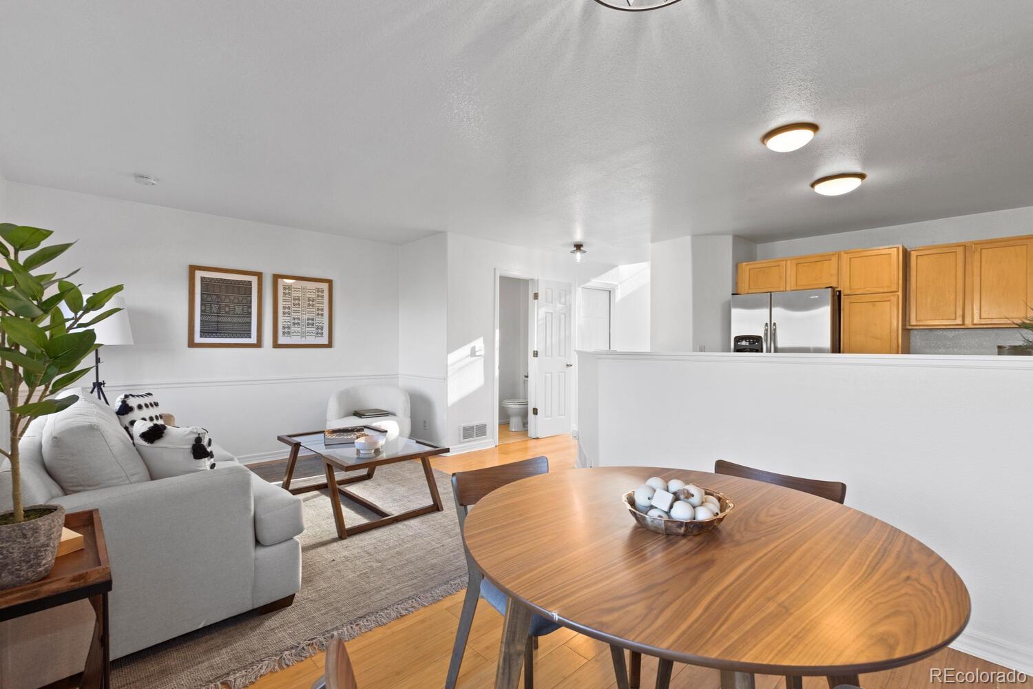 Open-plan living and dining area with a gray sofa, round wood table, and wood-cabinet kitchen.