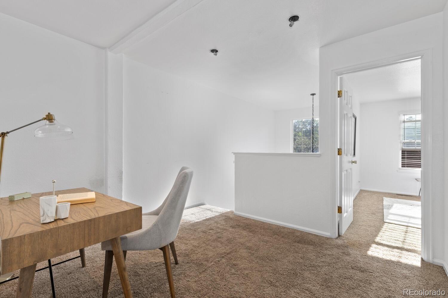 Carpeted upstairs loft with a wooden desk and chair beside an open doorway.