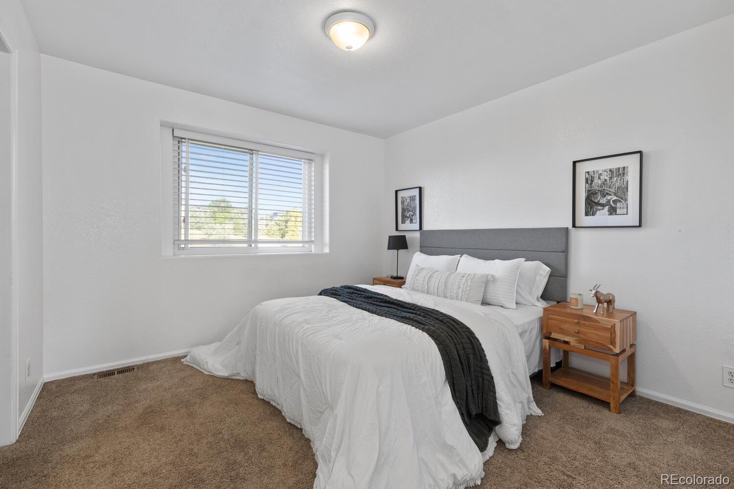 Bedroom with white bedding, a dark throw, gray headboard, and a window with horizontal blinds.