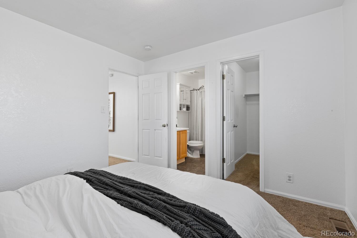 Staged bedroom with a dark knitted throw and open doors to the bathroom and closet.