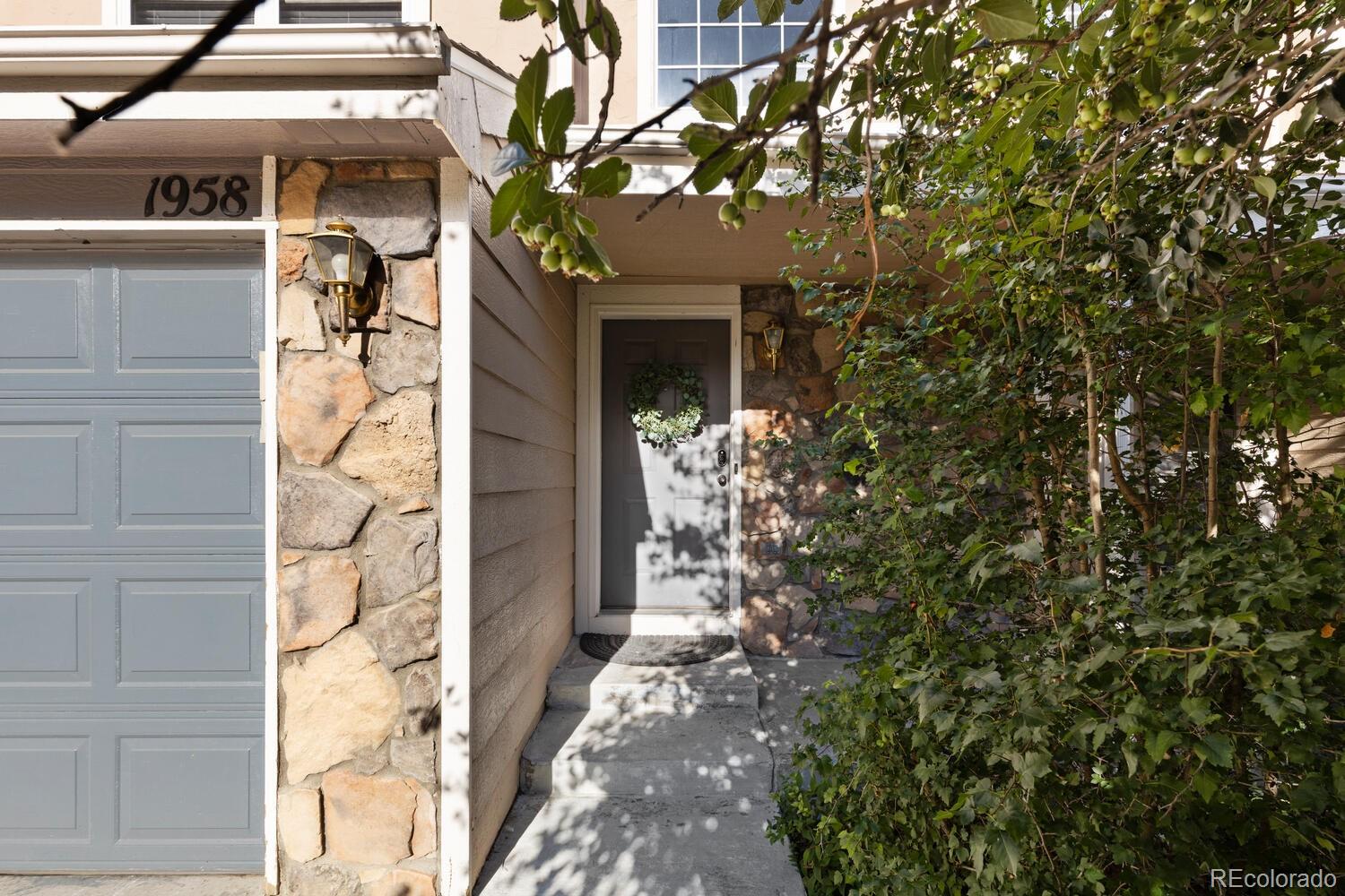 Home entrance with a gray wreath-adorned door, stone veneer, and leafy branches overhead.