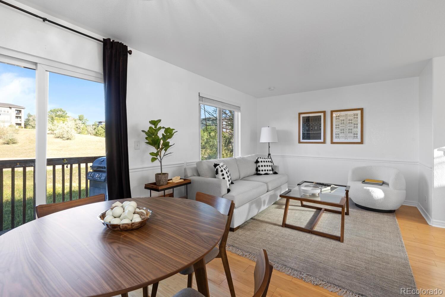 Living and dining room with a wood table, gray sofa, and windows overlooking a grassy slope.