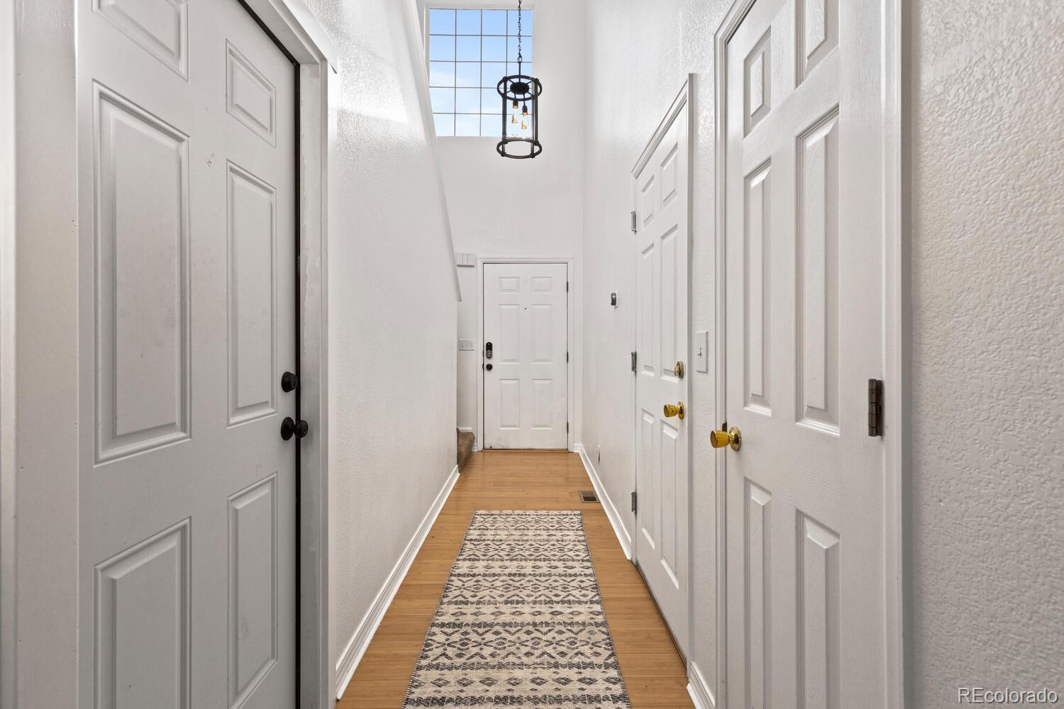 Bright entry hallway with white paneled doors, a patterned runner, and a tall window above the front door.