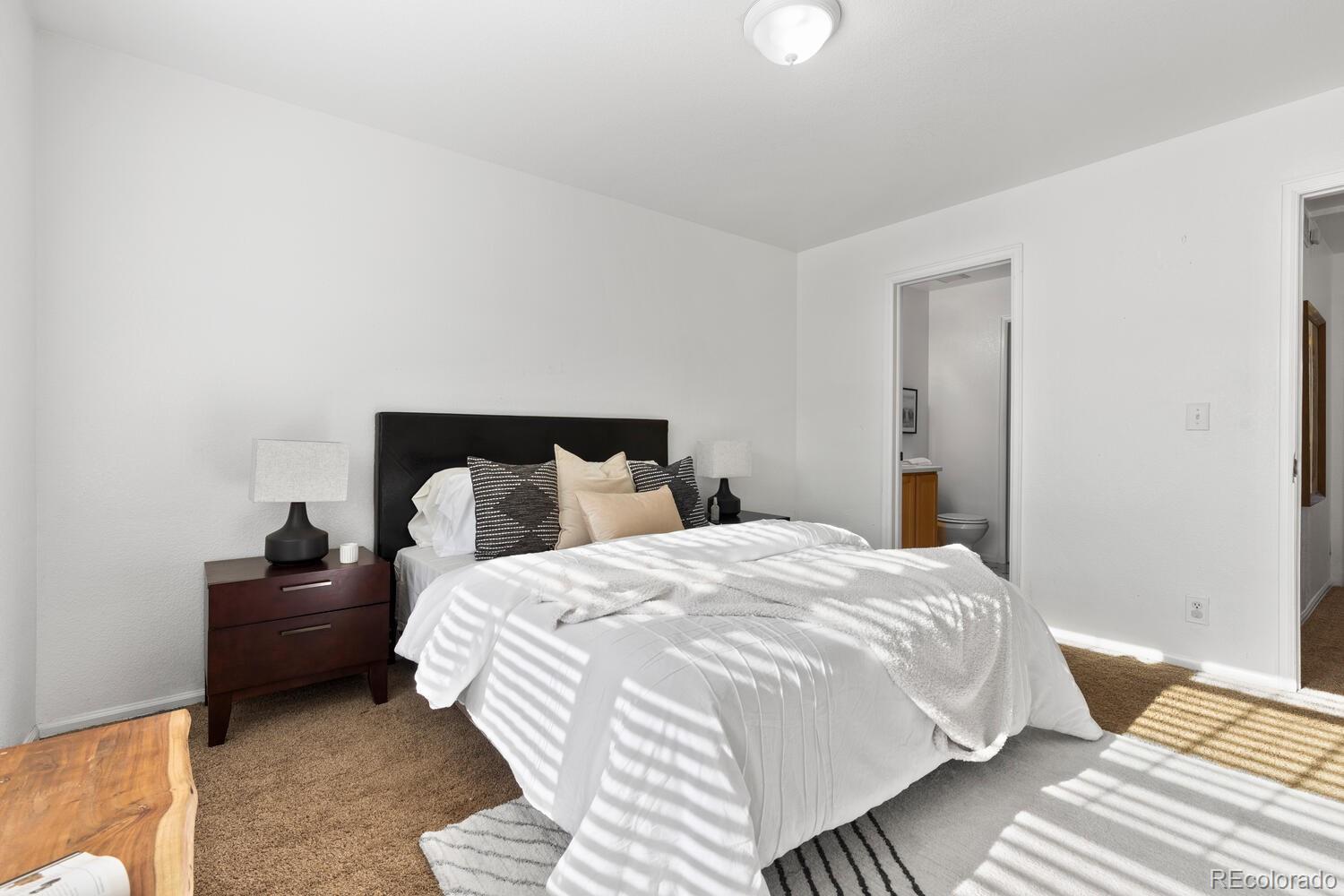 Furnished bedroom with a black headboard, striped rug, and sunlight across the bed.