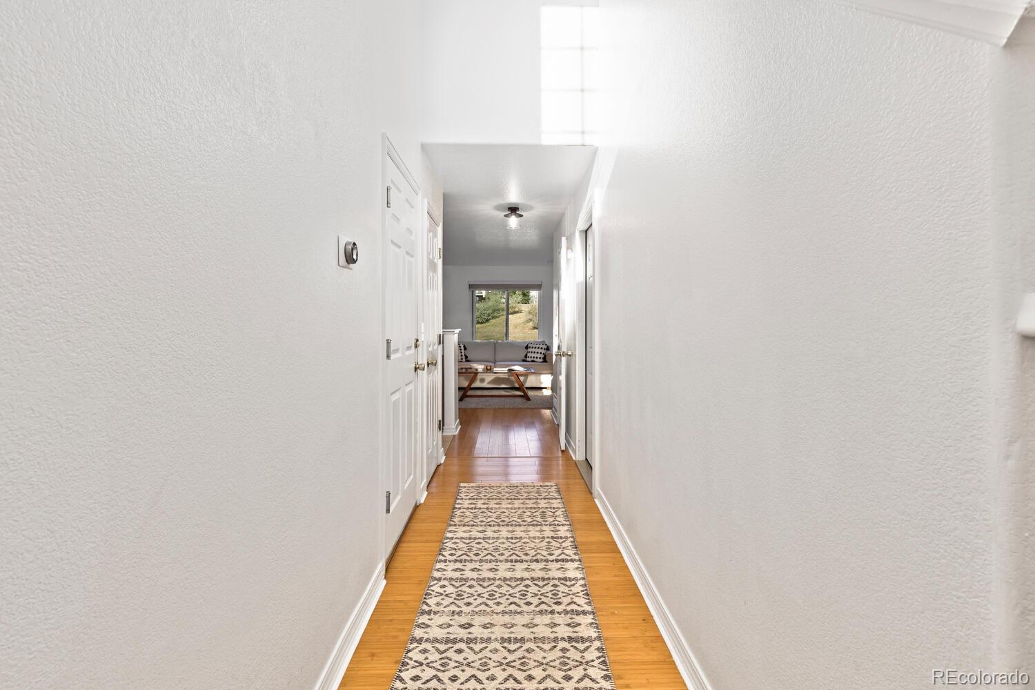 Bright hallway with hardwood floors and patterned runner leading to a sitting area by a window.