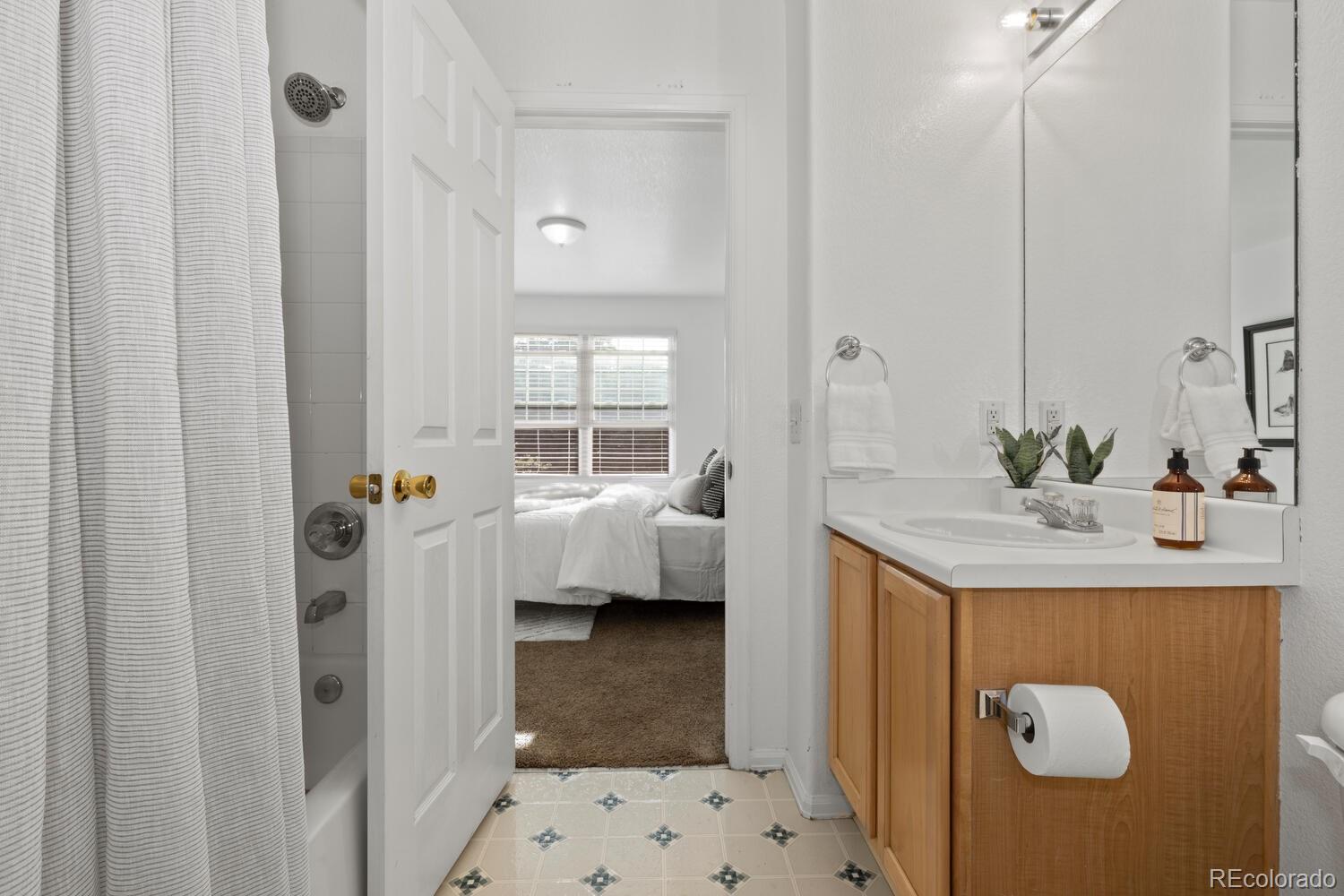 Bathroom with a light wood vanity and patterned tile floor, opening onto a bedroom.
