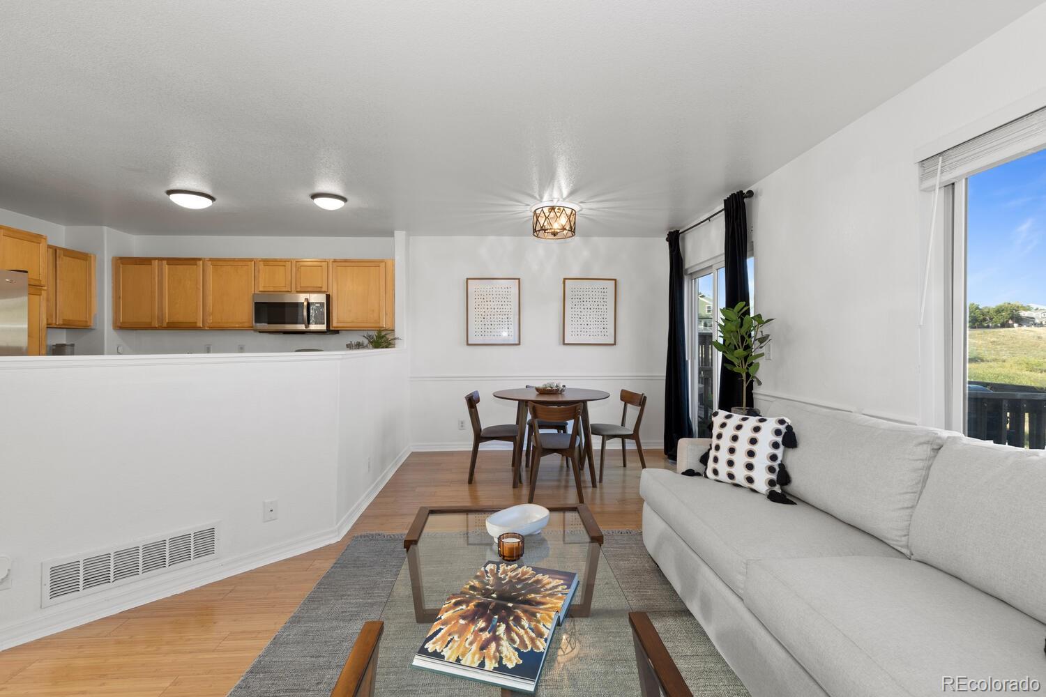 Open-plan living and dining room with a white sectional, glass coffee table, and light wood kitchen.