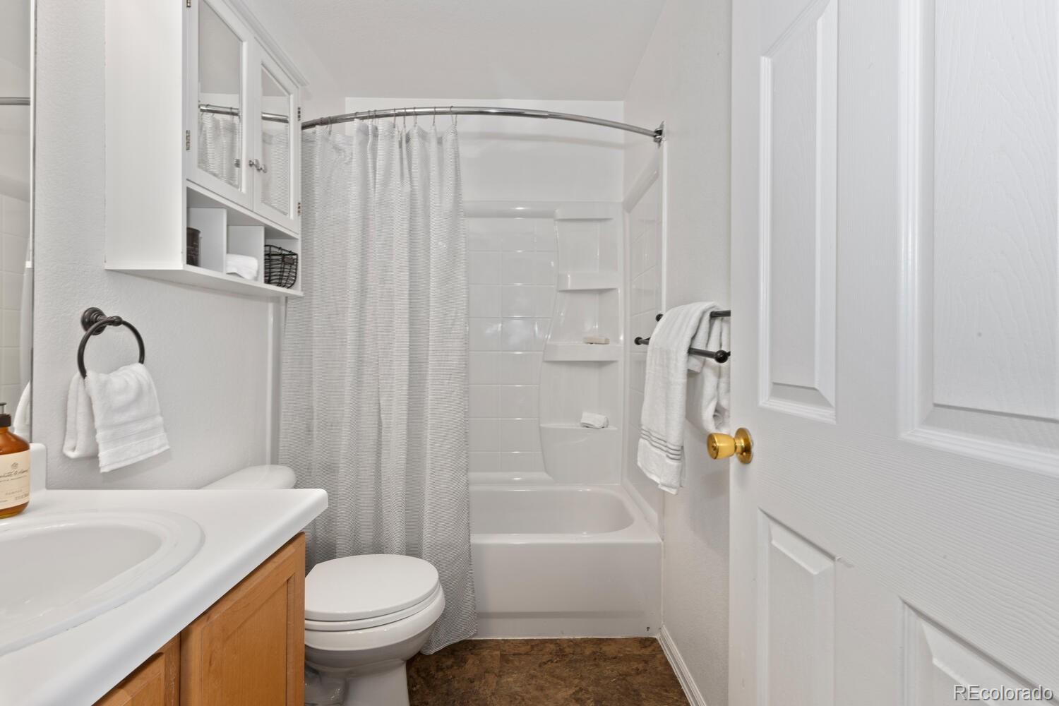 Bathroom with a curtained tub and shower, built-in storage, and a wood-front vanity.