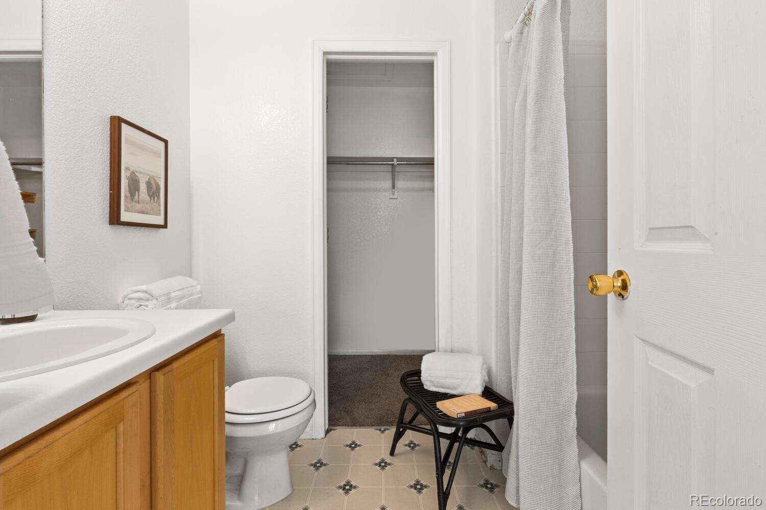 Bathroom with a wood vanity, tiled floor, and open doorway to a carpeted closet.