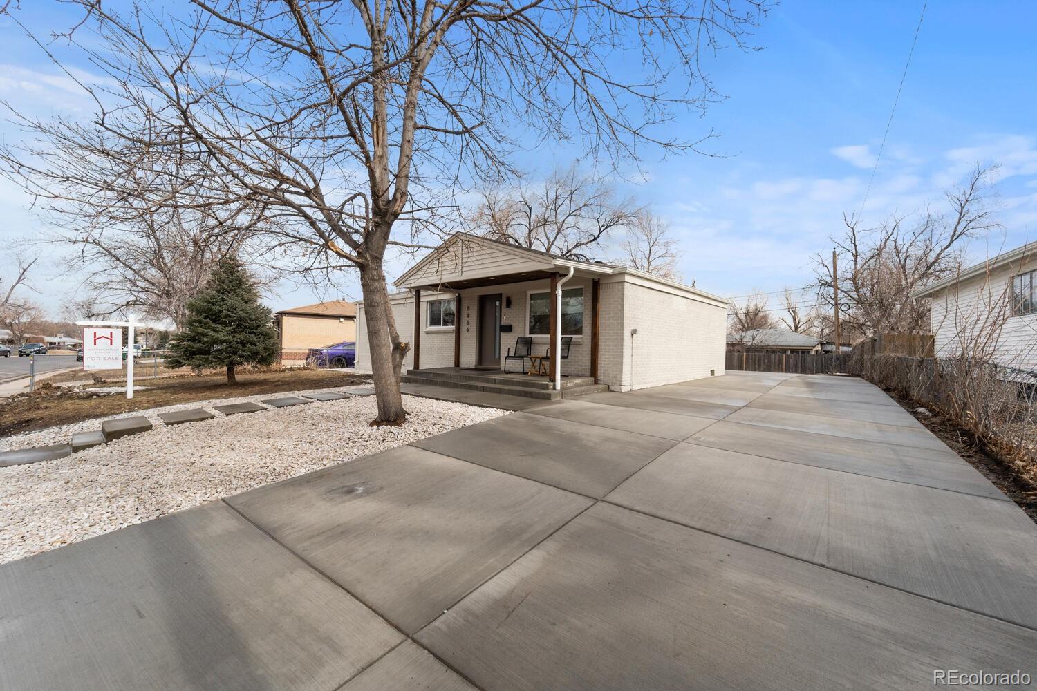 Single-story brick home with a covered porch, broad driveway, and white gravel landscaping.