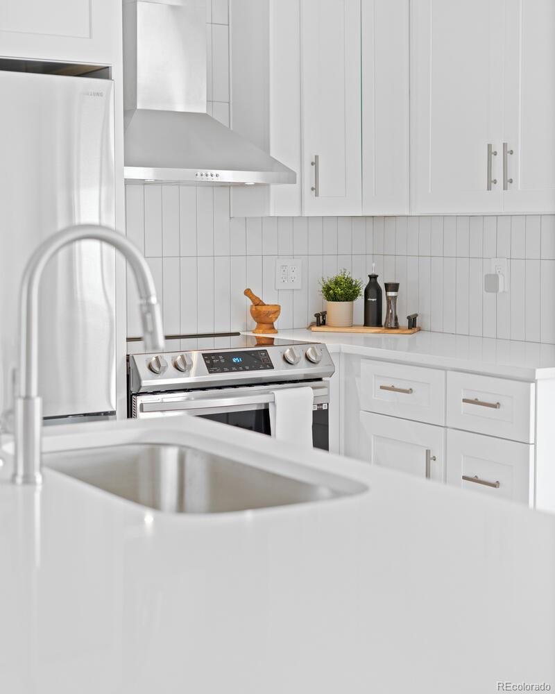 White kitchen with stainless appliances, tiled backsplash, and a large island sink.