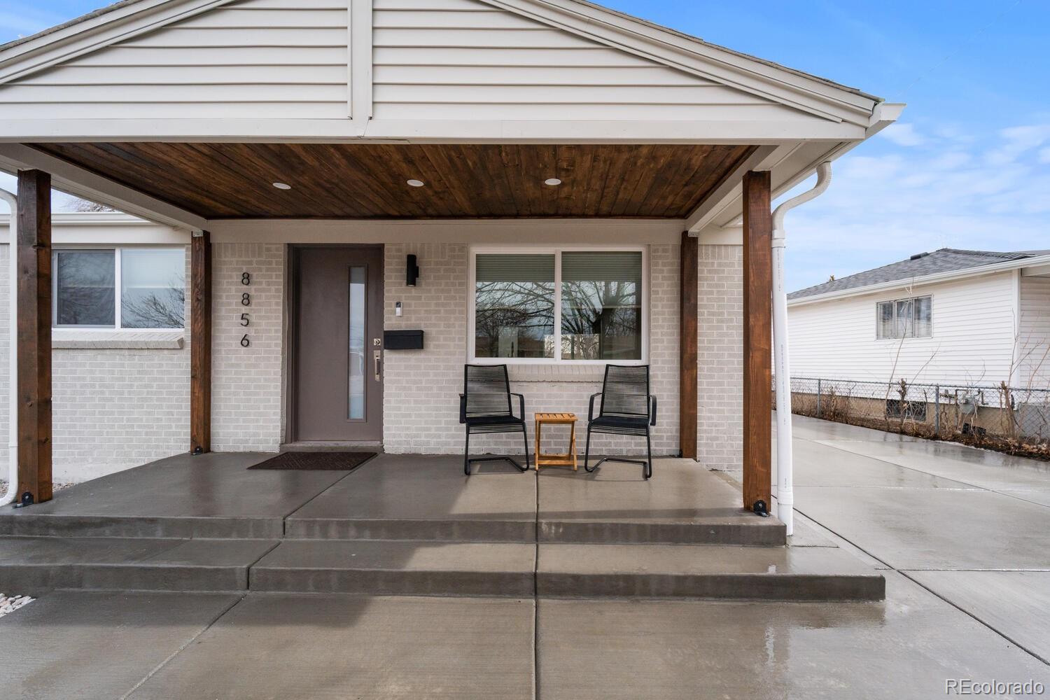 Home entrance with a covered porch, brick facade, dark wood posts, and two chairs.