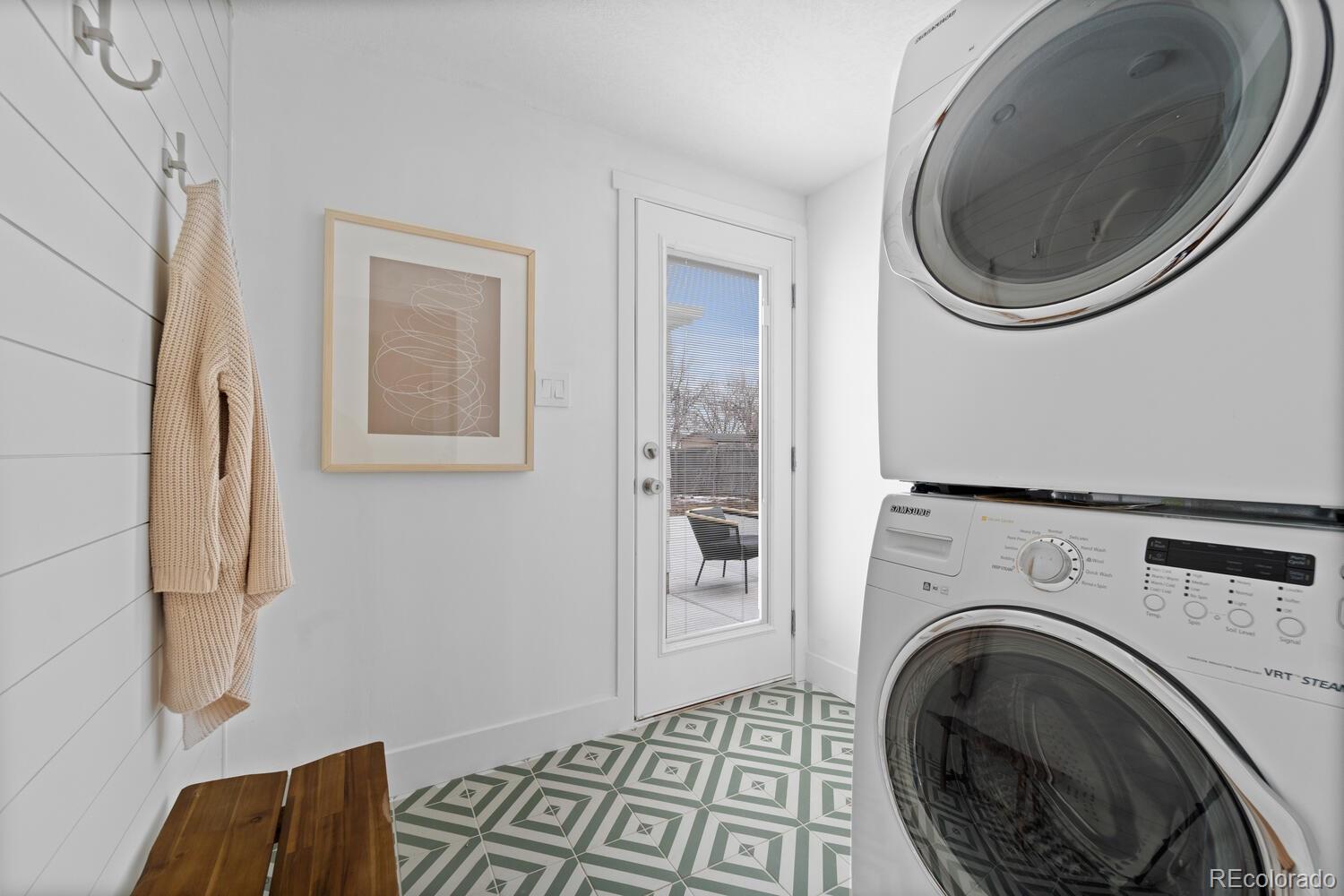 Laundry room with stacked washer and dryer, patterned tile floor, and glass patio door.