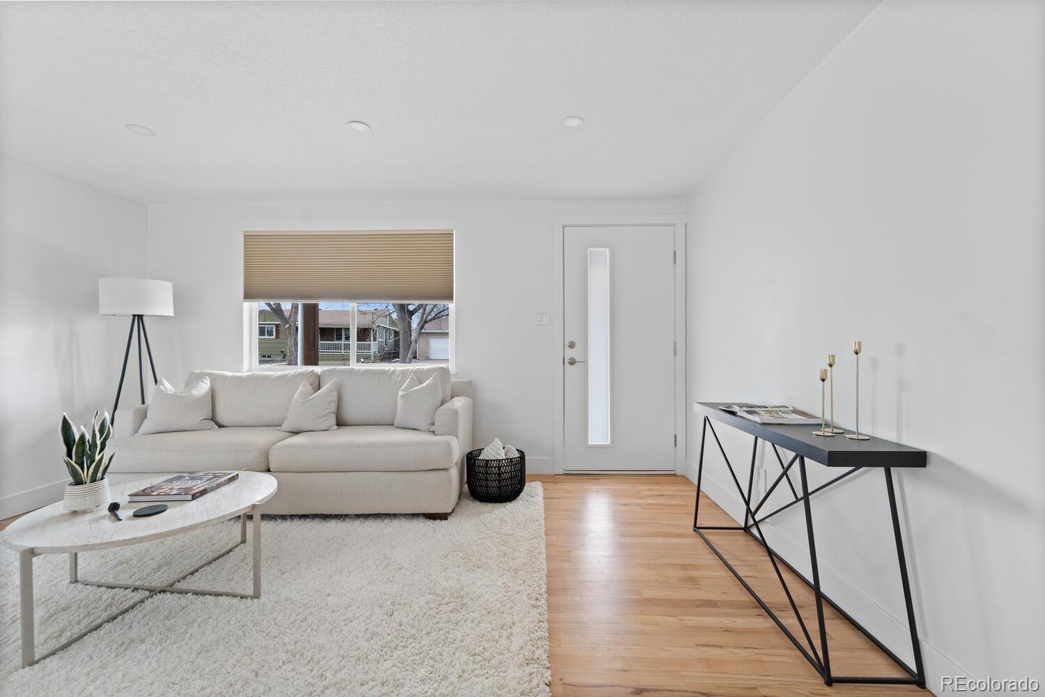 Staged living room with a white sofa, pale rug, and hardwood floors beside the front door.