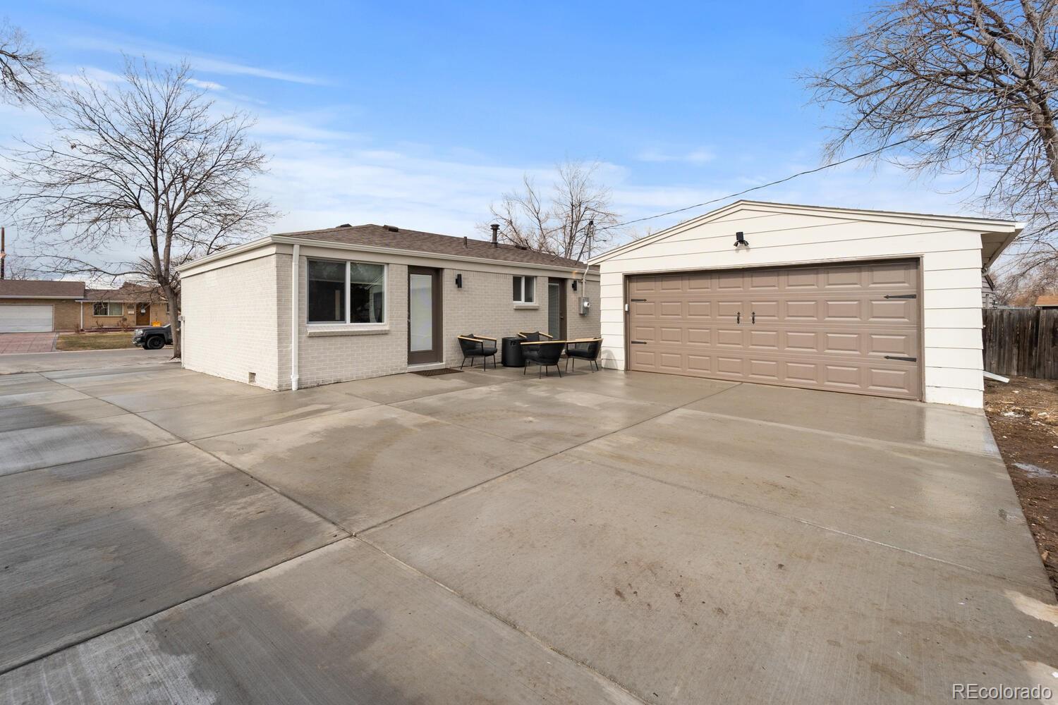 Single-story brick home and detached two-car garage with a wide concrete driveway and outdoor seating.