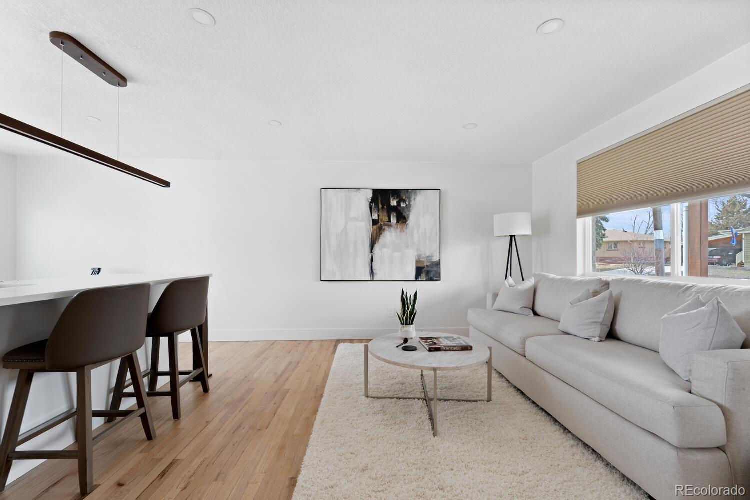 Staged living room with a light gray sectional, abstract art, light wood floors, and a breakfast bar.