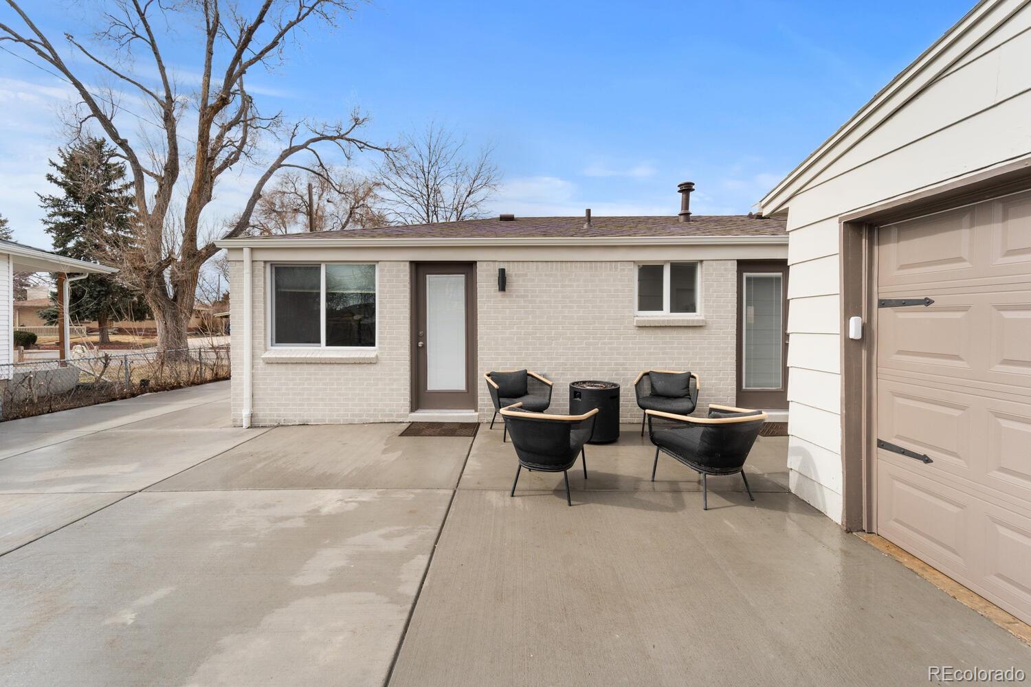 Rear patio with black chairs around a fire pit beside a light brick home and garage.