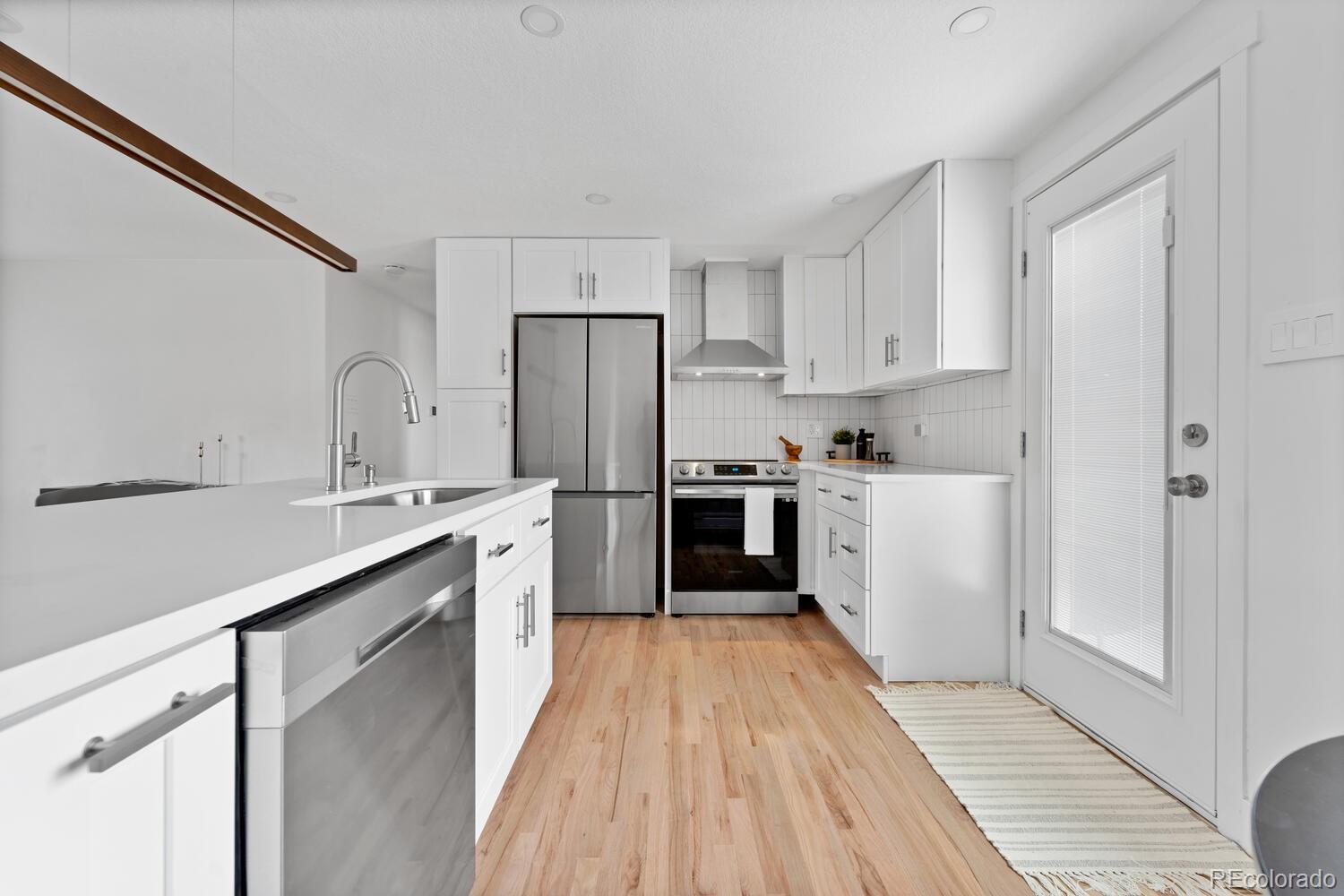 Bright white kitchen with stainless steel appliances, a large island, and light wood flooring.