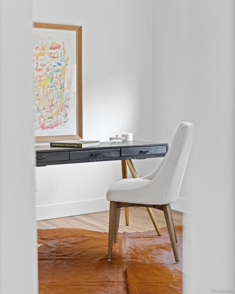 Home office with a dark desk, white chair, framed abstract art, and brown hide rug.