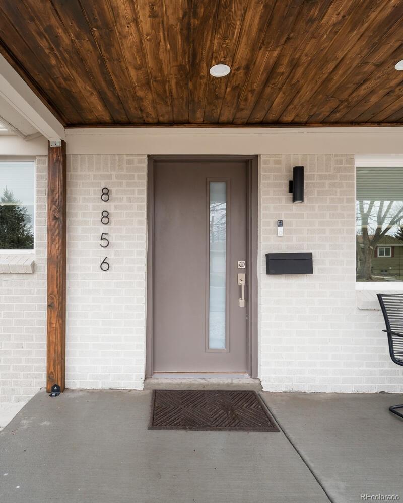 Home entry with a taupe door, light brick facade, and wood-plank porch ceiling.