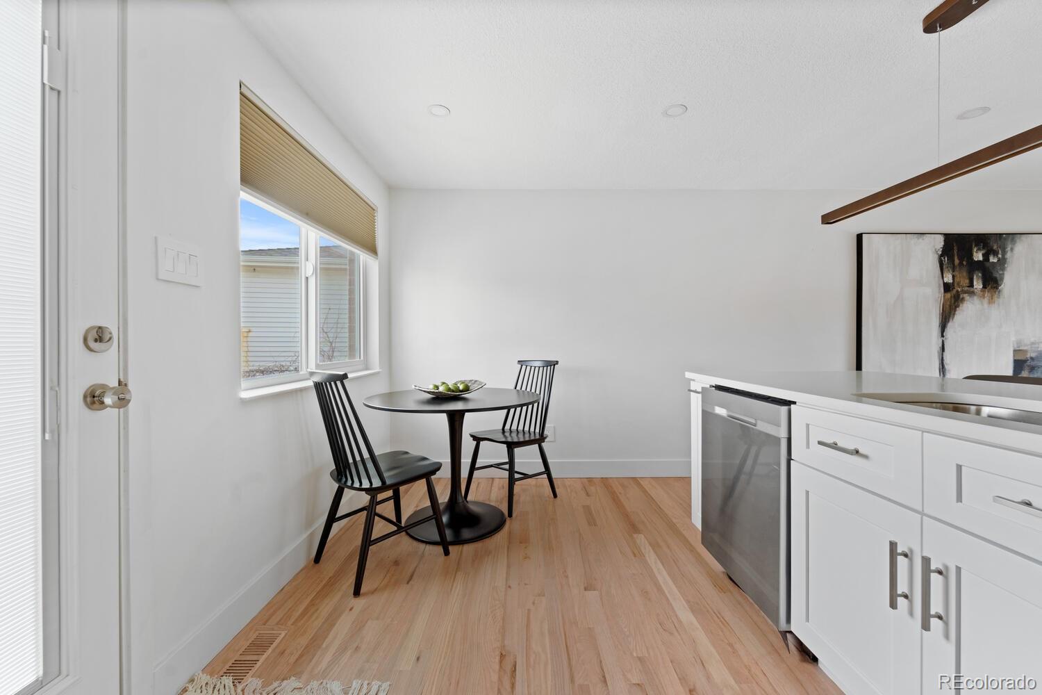 Kitchen dining nook with white cabinetry, light wood floors, and a round table beside the window.