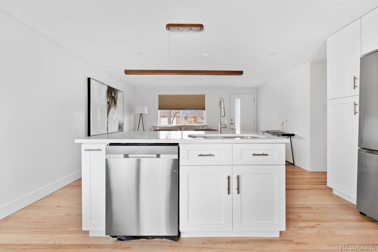Bright kitchen with white cabinetry, stainless-steel dishwasher, and a large island opening to living area.