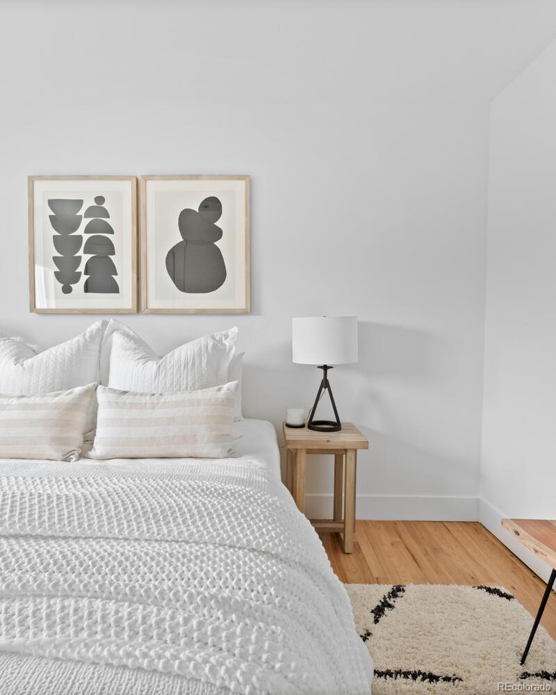 Staged bedroom with a white quilted bed, abstract wall art, and a wooden bedside table.